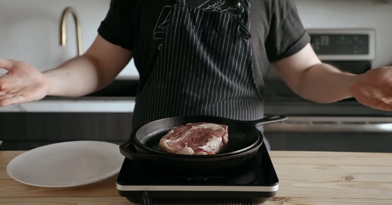 Chef in a kitchen standing in front of a iron skillet with steak inside cooking